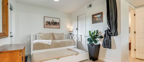 A bedroom with a bed, a dresser, a plant, and a painting on the wall.