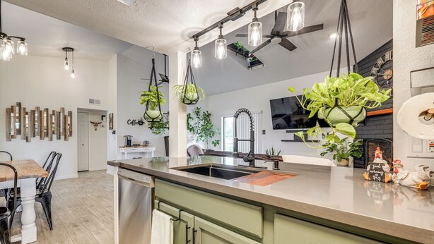 A modern kitchen with a large island, hanging plants, and a dining area with a wooden table and chairs. - Family Home on > 2 Acres w/ Stables in Gilbert! (Gilbert)