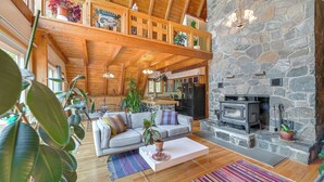 A spacious living area with a stone fireplace, wooden beams, and a high ceiling.