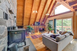 Ein gemütliches Wohnzimmer mit Kamin aus Stein, Holzbalken und großen Fenstern.