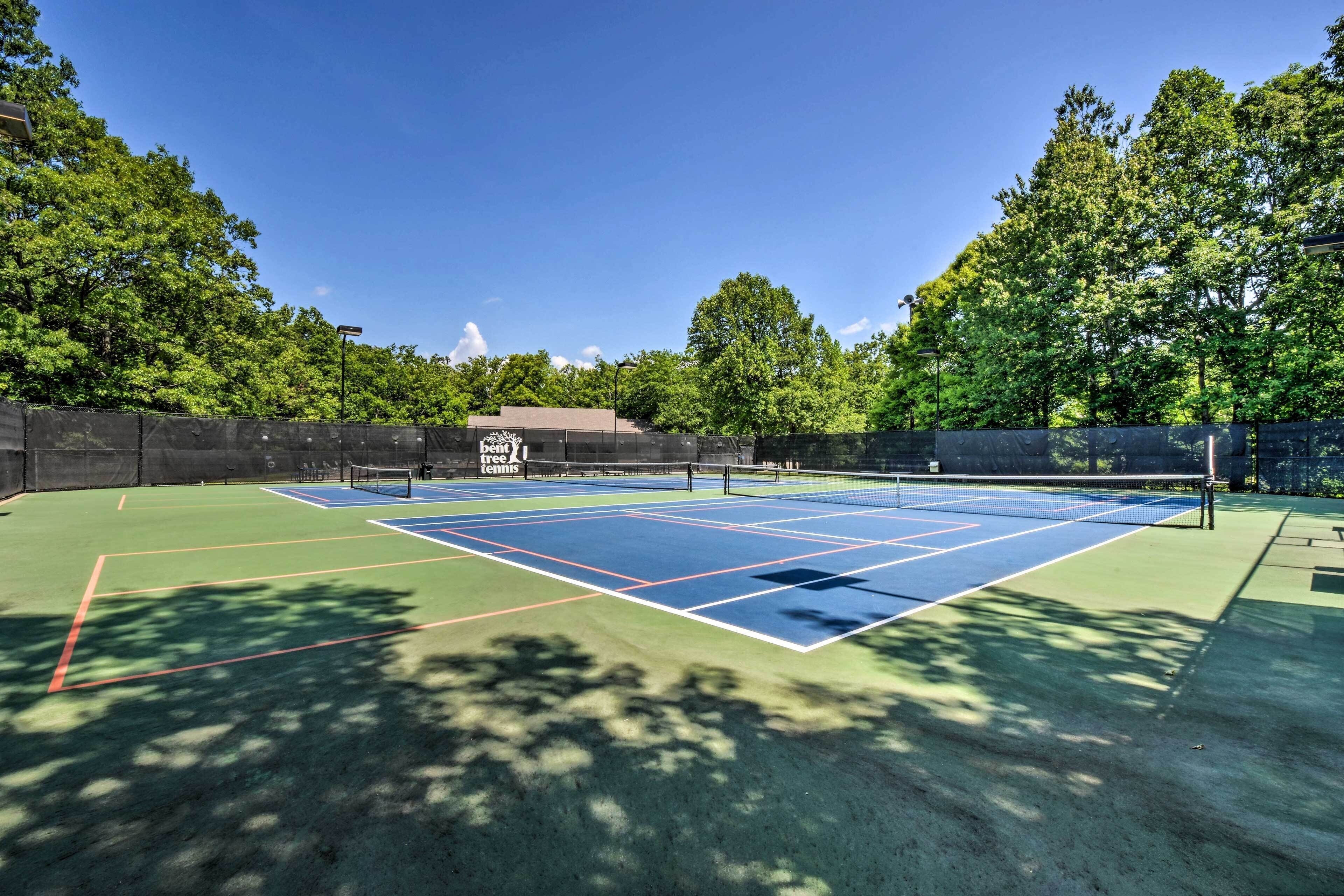 An outdoor tennis court with a net, surrounded by trees and a fence.