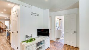 A modern living room with a flat-screen TV on a wooden console, a staircase leading to another room, and a white door with a mirror and towel rack. - York Farmhouse Hideaway Near Lake Redman (York)