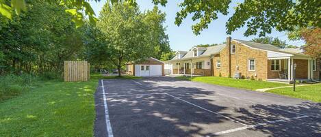 A residential street with a paved driveway, a garage, and a brick house with a porch.