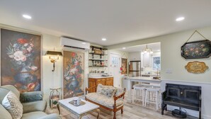 A living room with a sofa, a coffee table, a fireplace, and a dining area with a kitchen in the background. - Hot Tub & Fenced Yard: Cozy Cottage Grove Home (Cottage Grove)