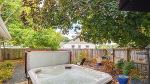 A hot tub in a backyard with a wooden fence and trees. - Hot Tub & Fenced Yard: Cozy Cottage Grove Home (Cottage Grove)