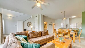 A spacious living room with a brown sofa, a wooden dining table, and a ceiling fan. - Townhouse in Lake Berkley Resort! 5 Mi to Old Town (Kissimmee)