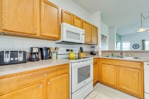 A kitchen with wooden cabinets, a white microwave, a stove, and a sink. - Townhouse in Lake Berkley Resort! 5 Mi to Old Town (Kissimmee)