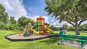 A playground with multiple slides and a climbing structure, surrounded by grass and trees. - Townhouse in Lake Berkley Resort! 5 Mi to Old Town (Kissimmee)