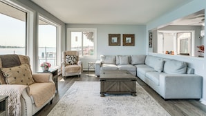 A spacious living room with a large window, a grey sofa, a beige armchair, and a wooden coffee table. - Spacious Riverfront Home w/ Dock in St Clair! (St. Clair)