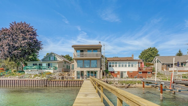 A wooden pier leading to a modern two-story building with a balcony, situated by a clear waterfront. - Spacious Riverfront Home w/ Dock in St Clair! (St. Clair)
