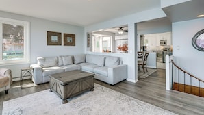 A spacious living room with a sectional sofa, a wooden coffee table, and a large window. A kitchen is visible in the background. - Spacious Riverfront Home w/ Dock in St Clair! (St. Clair)