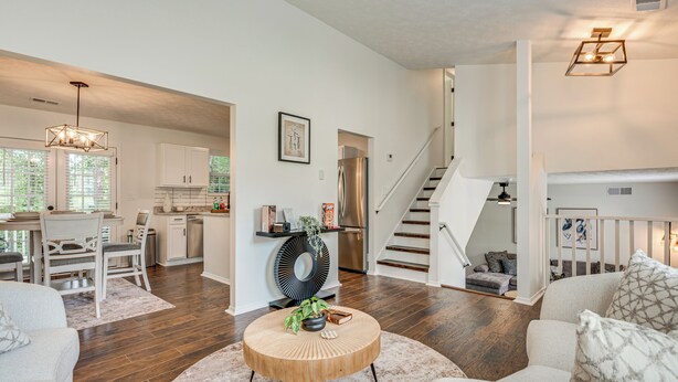 Een moderne woonkamer met een ronde salontafel, een eethoek met een witte tafel en stoelen, en een keuken met witte kasten en roestvrijstalen apparatuur.