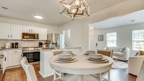 Een moderne keuken met witte kasten, een inbouwoven en een eethoek met een ronde tafel en stoelen.