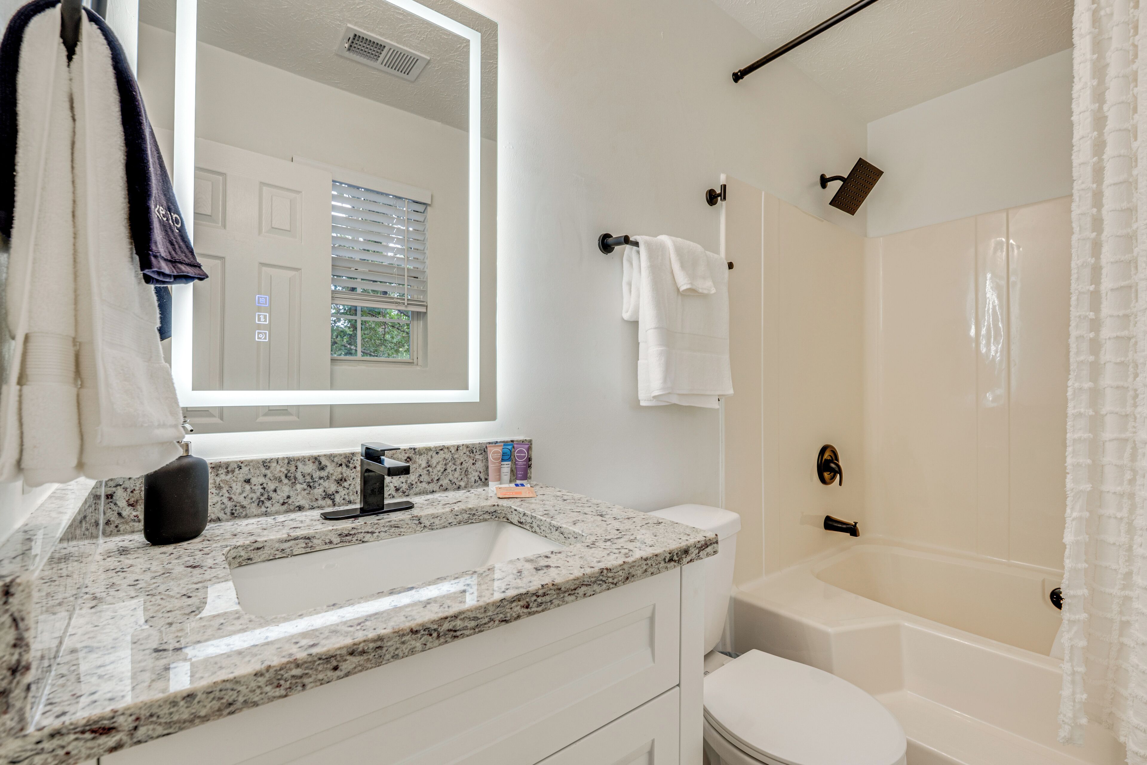 A modern bathroom with a granite countertop sink, white vanity, a large mirror, a bathtub, and a shower curtain.