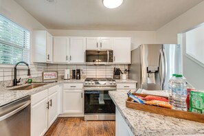 Une cuisine moderne avec des armoires blanches, des appareils en acier inoxydable et un plancher en bois.