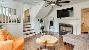 Een moderne woonkamer met een open haard, een plafondventilator en een tv erboven.