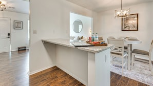 Een moderne keuken met een granieten aanrecht, een eethoek met witte stoelen en een hanglamp.