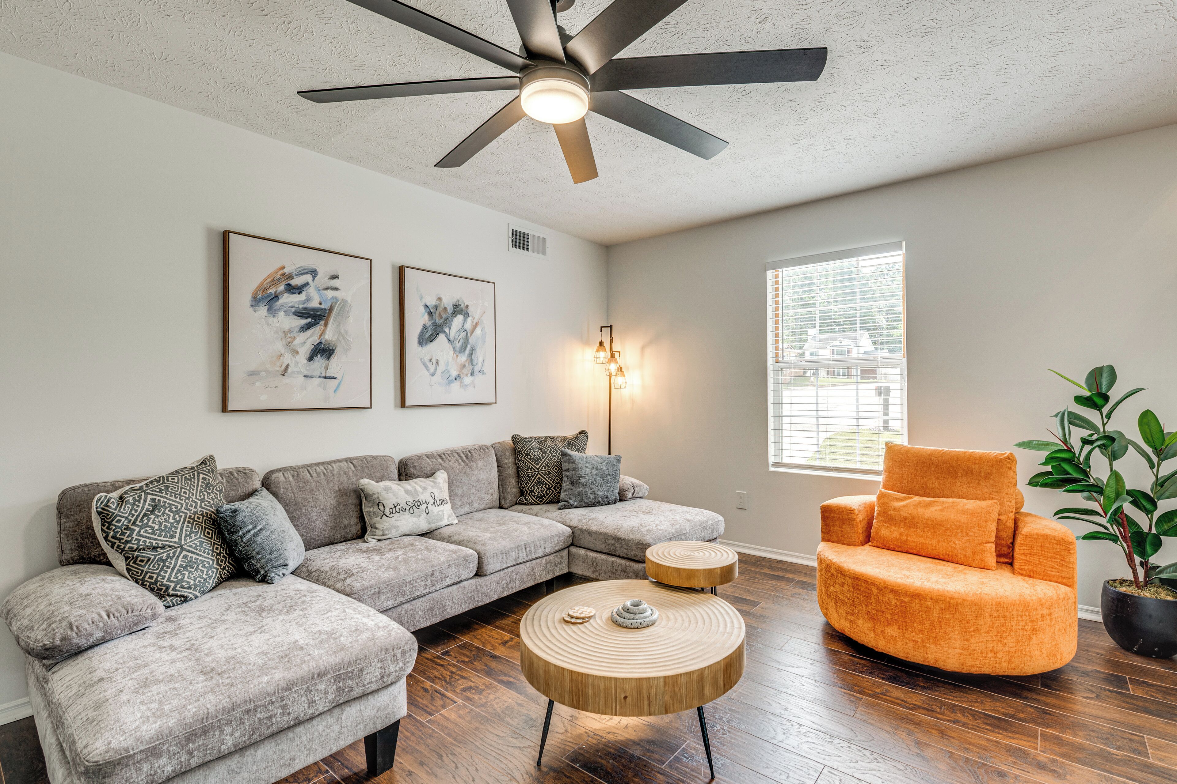 A modern living room with a grey sectional sofa, an orange armchair, a round wooden coffee table, and a ceiling fan.