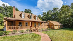 A two-story wooden house with a covered porch, a brick pathway leading to the entrance, and a small detached garage. - 11 Mi to Fort Lee: 5-acre Retreat w/ Scenic Views (Petersburg)
