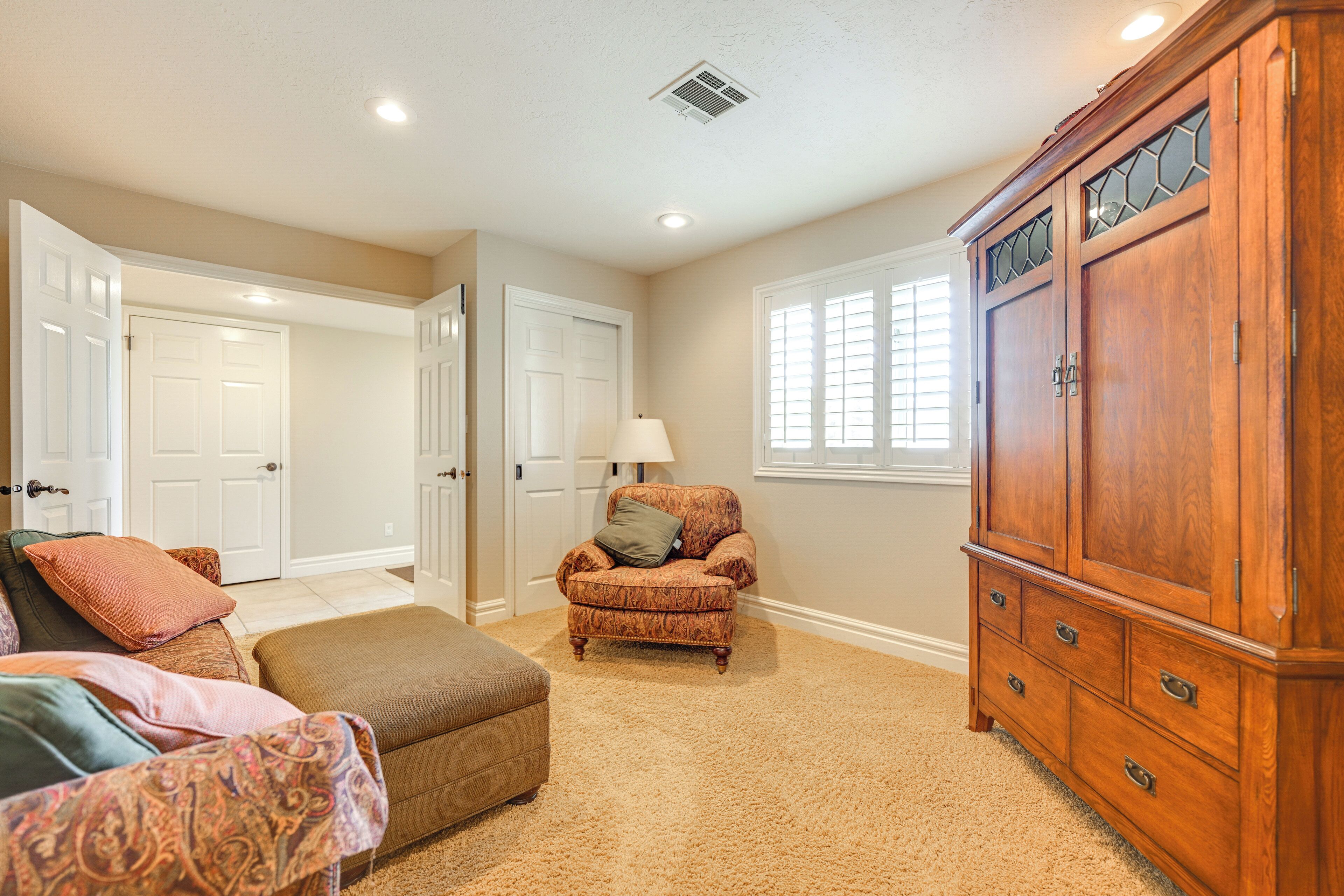 A spacious room with a large wooden cabinet, a patterned armchair, and a beige carpet.