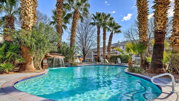 A swimming pool surrounded by palm trees and a small waterfall feature. - Golf Getaway 5 Mi to Dtwn: Las Palmas Resort Condo (St. George)