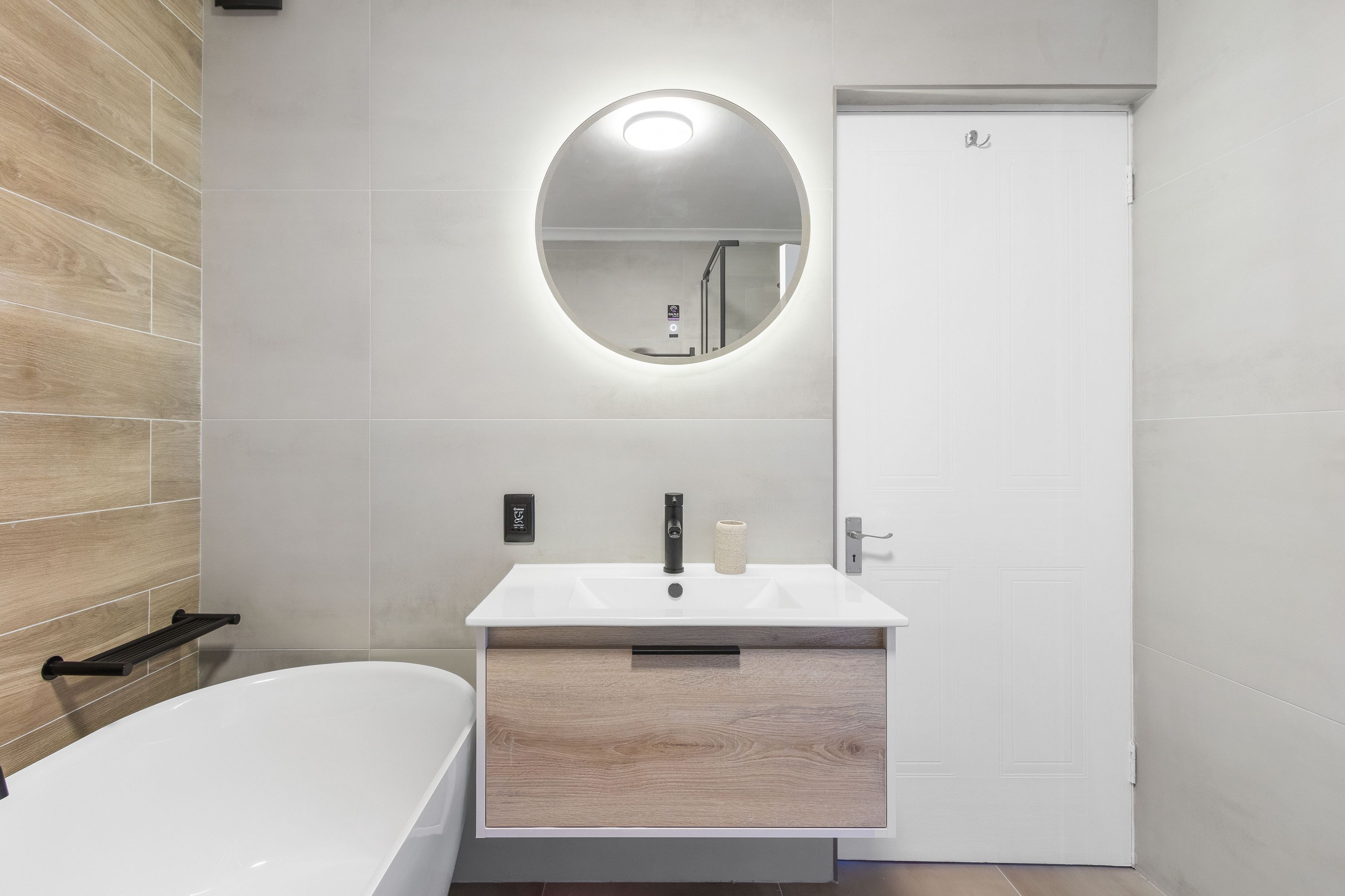 A modern bathroom with a white sink, a round mirror, and a bathtub.