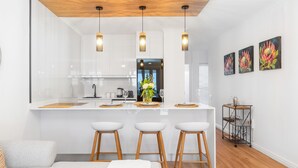 Una cocina moderna con armarios blancos, una isla central con taburetes, iluminación colgante y una obra de arte en la pared.