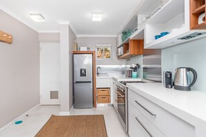 Une cuisine moderne avec des meubles blancs, des appareils en acier inoxydable et une fenêtre qui laisse entrer la lumière naturelle.