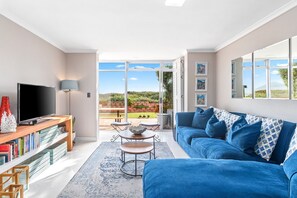 A modern living room with a blue sofa, a flat-screen TV, and a bookshelf. - Neptune Isle 9 (Cape Town)
