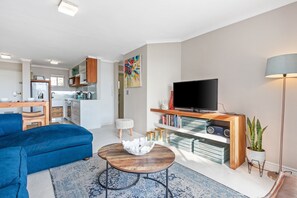Un salon moderne avec un canapé bleu, une table basse, un téléviseur et une bibliothèque.
