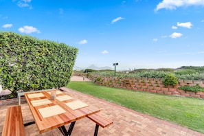 A wooden table with benches in a garden area with a brick wall and a hedge.