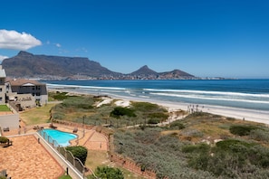 A coastal property with a swimming pool, a fenced patio area, and a view of the ocean and mountains.