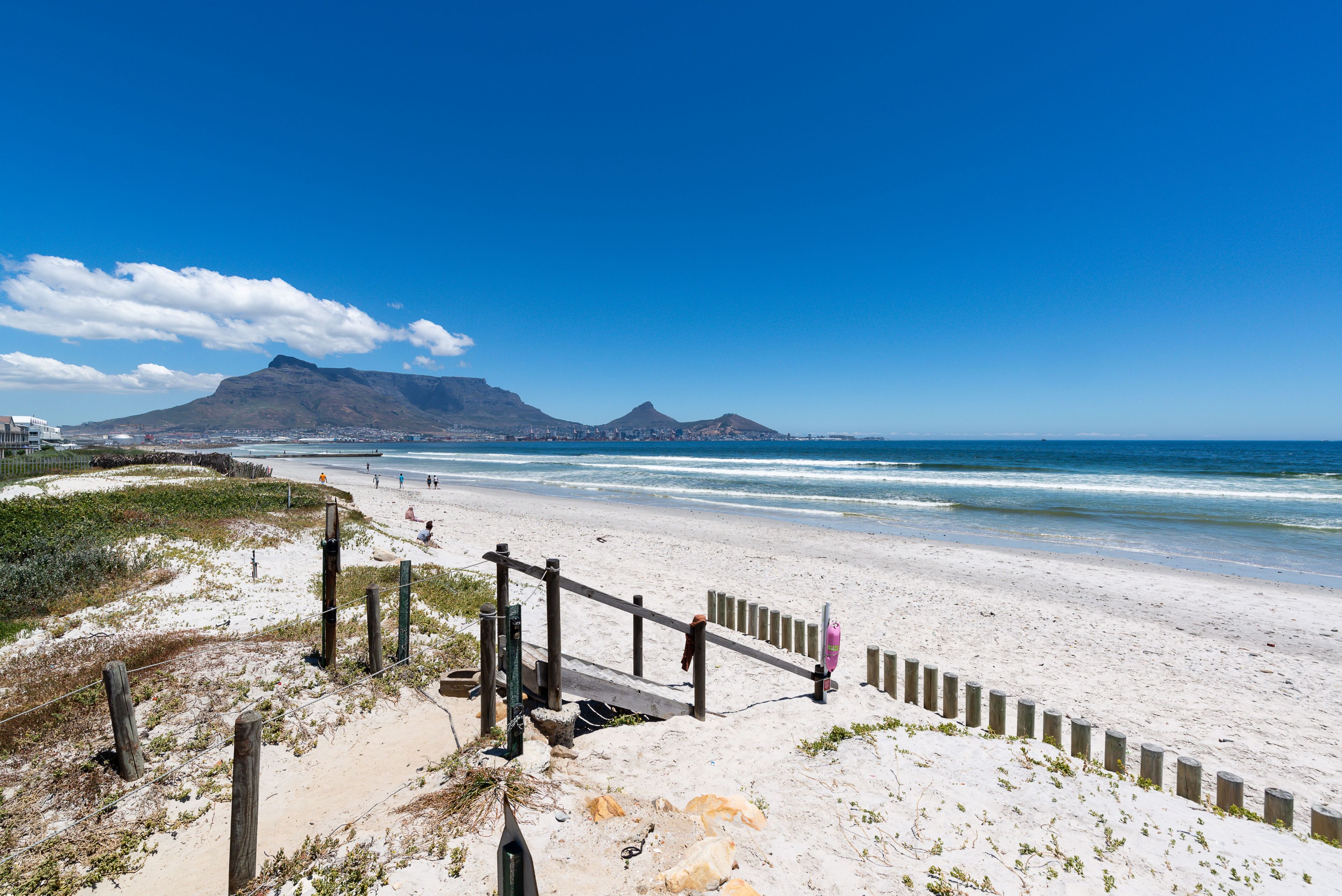 A beach with a wooden fence, sandy dunes, and a mountain in the background.