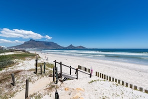 Ein Strand mit Holzzaun, Sanddünen und einem Berg im Hintergrund.