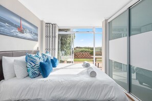 A modern hotel room with a large bed, white linens, blue patterned pillows, and a painting of sailboats on the wall. - Neptune Isle 9 (Cape Town)