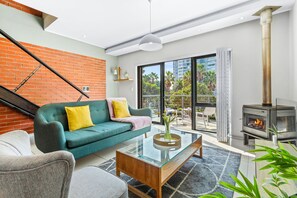 A modern living room with a green sofa, a glass coffee table, and a wood-burning stove. - Manhattan Wharfside 301 (Cape Town)