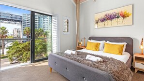 A modern bedroom with a large bed, a city view, and a painting on the wall. - Manhattan Wharfside 301 (Cape Town)