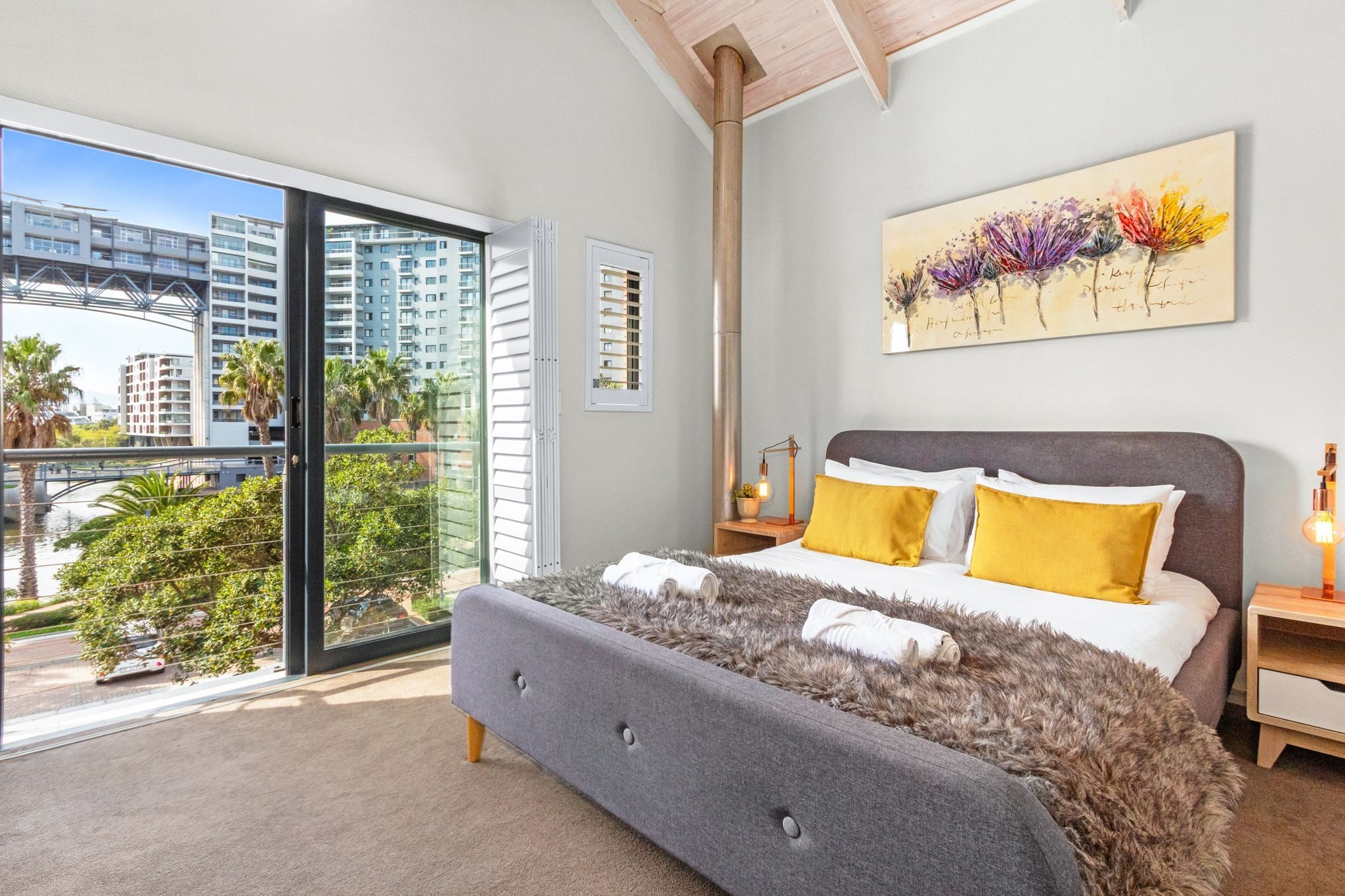 A modern bedroom with a large bed, a city view, and a painting on the wall.