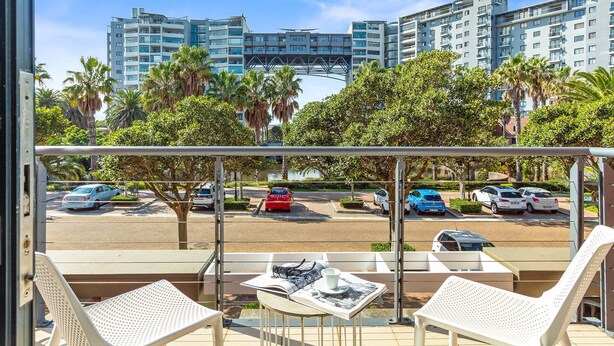 A balcony with white chairs and a table, overlooking a parking area with several cars and palm trees. - Manhattan Wharfside 301 (Cape Town)