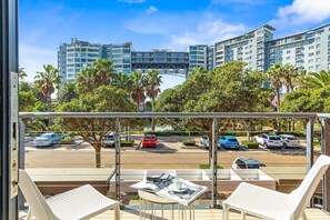 A balcony with white chairs and a table, overlooking a parking area with several cars and palm trees. - Manhattan Wharfside 301 (Cape Town)