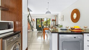 A modern kitchen with a built-in washer and dryer, a dining area with a table and chairs, and a staircase leading to another level. - Manhattan Wharfside 301 (Cape Town)