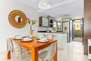 A modern dining area with a wooden table set for four, clear chairs, and a decorative mirror on the wall. - Manhattan Wharfside 301 (Cape Town)