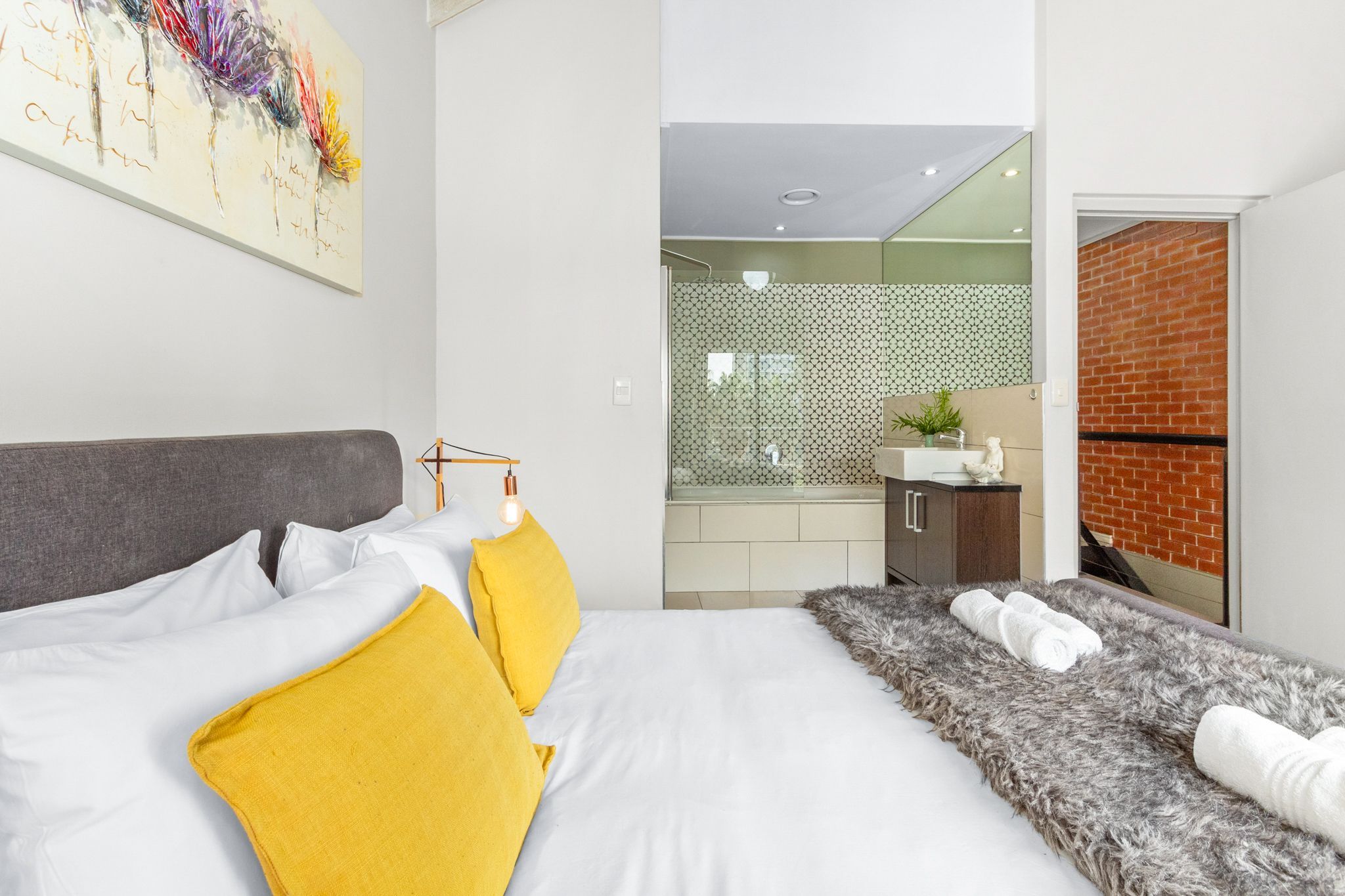 A modern hotel room with a bed, a fluffy rug, and a bathroom visible through an open door.