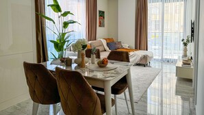 Una sala de estar moderna con comedor, ventanas amplias con cortinas translúcidas, un sofá con cojines y una mesa de centro con adornos.