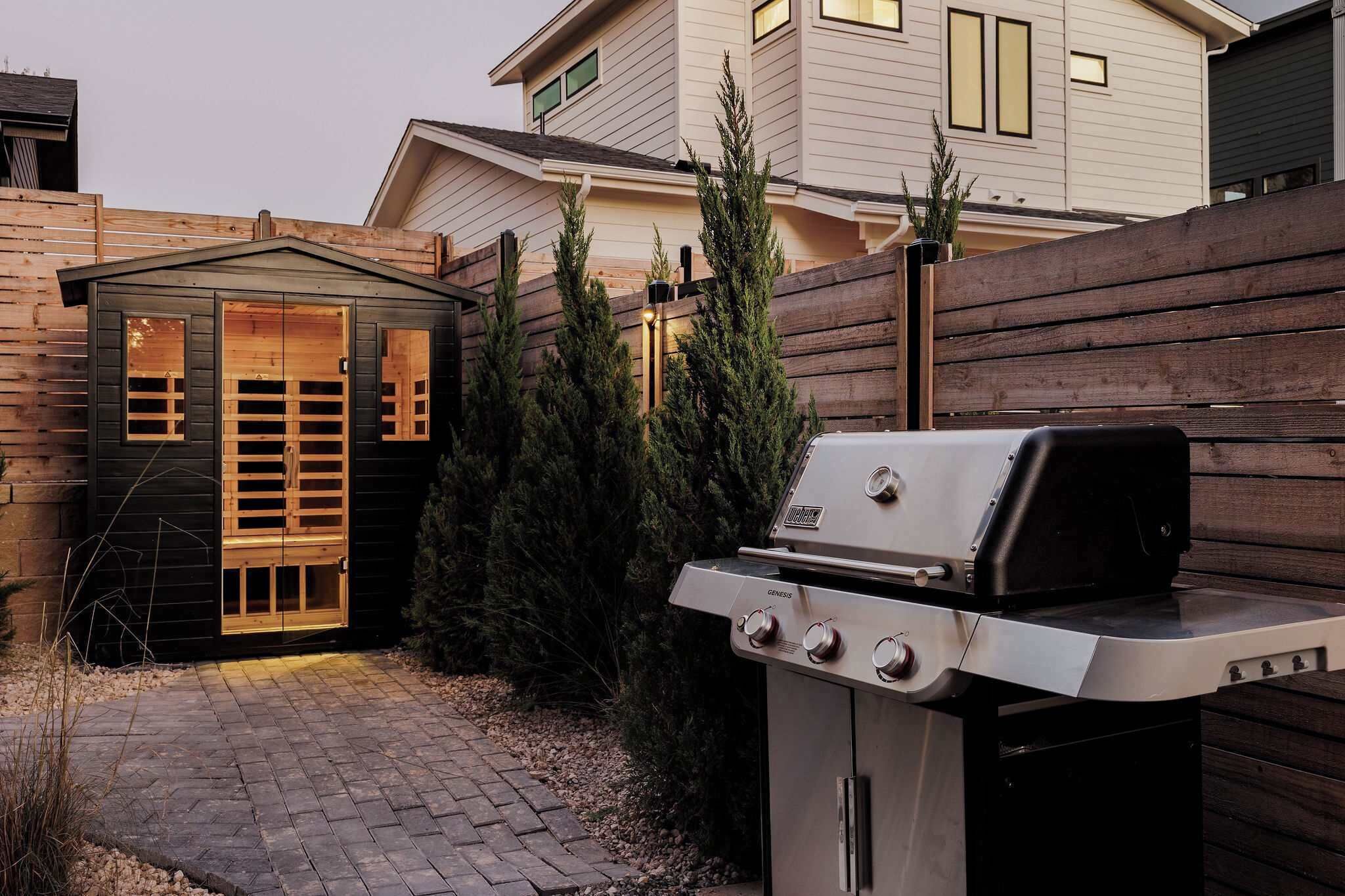A backyard with a wooden shed, a barbecue grill, and a house in the background.