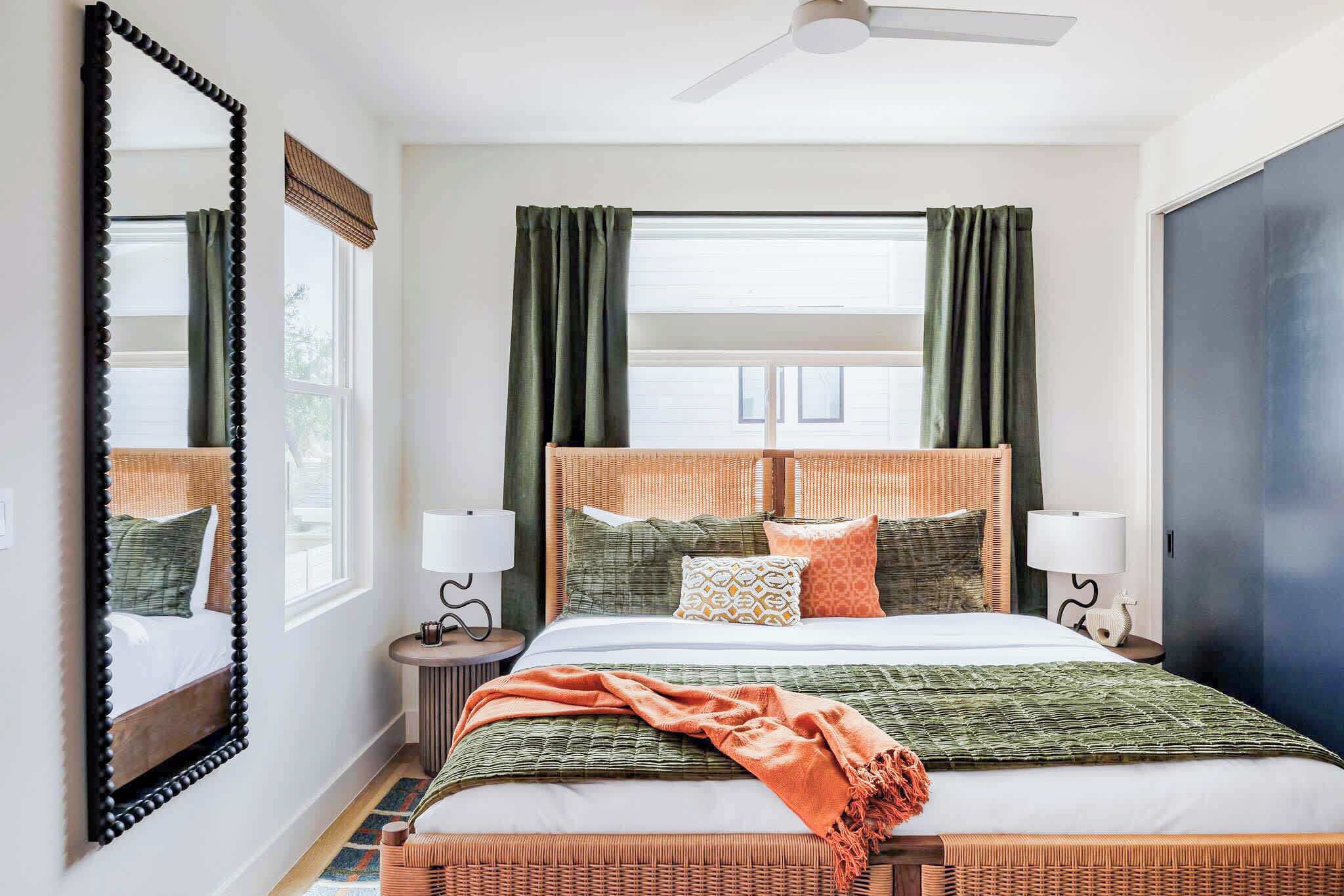 A hotel room with a bed, two bedside tables, a mirror, a ceiling fan, and a window with curtains.