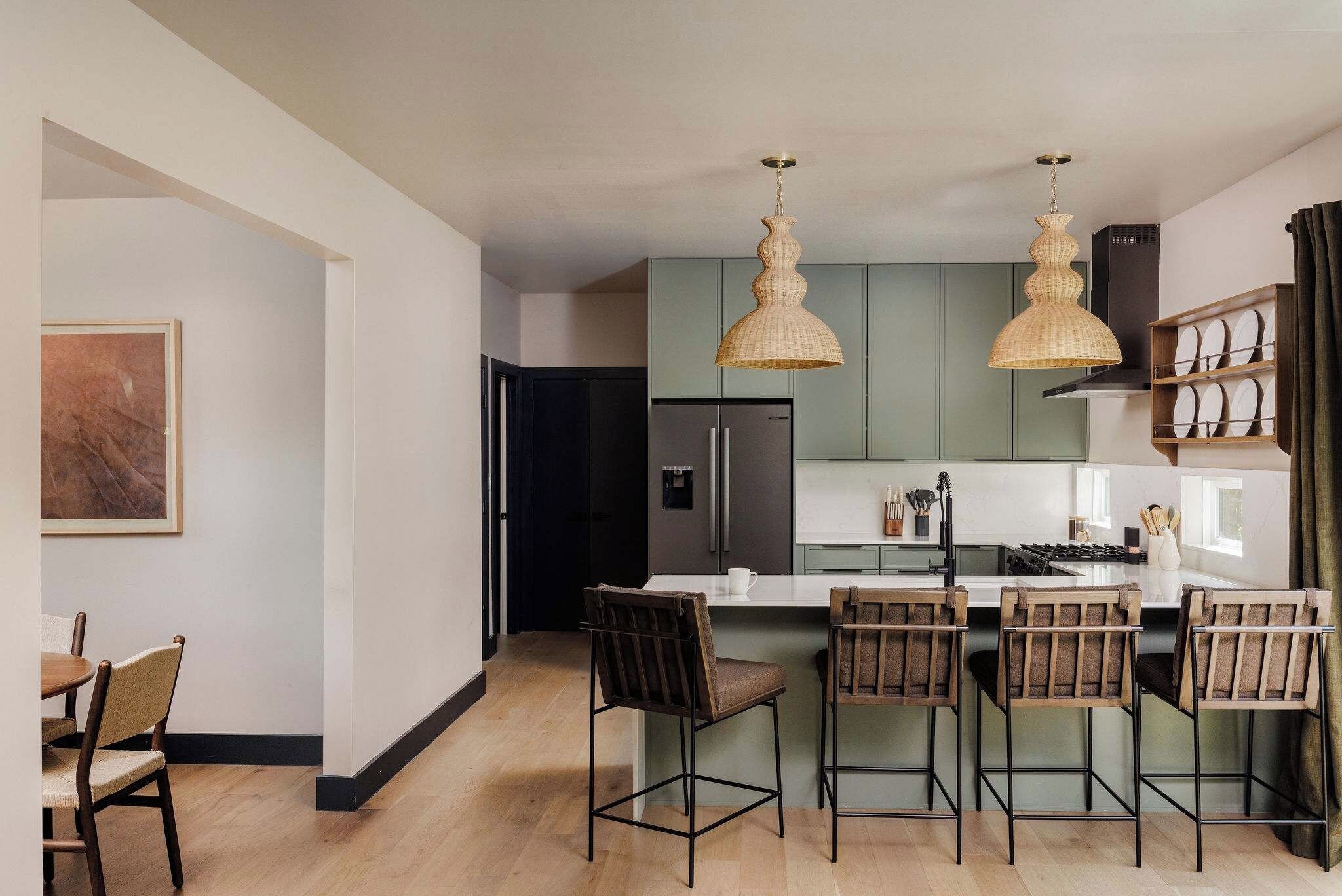 A modern kitchen with a central island, bar stools, pendant lighting, and a dining area with a table and chairs.