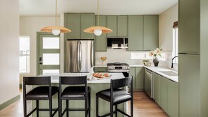 Una cocina moderna con gabinetes verdes, una isla central con sillas, una estufa y luces colgantes.