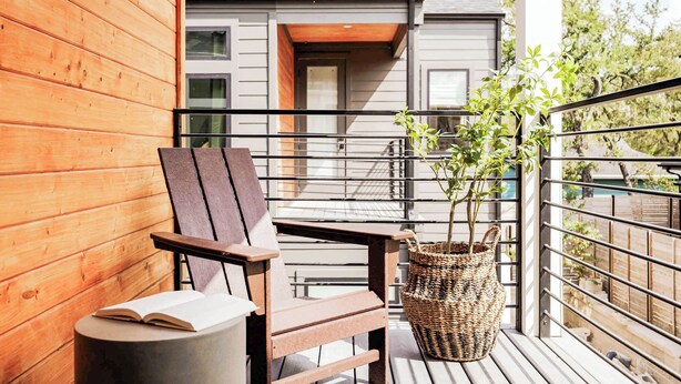 Una terraza de madera con una silla y una planta en maceta, con vista a un edificio moderno.