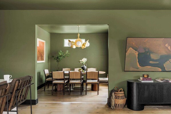 Un coin repas avec une table ronde, des chaises, un luminaire suspendu et un tableau au mur.